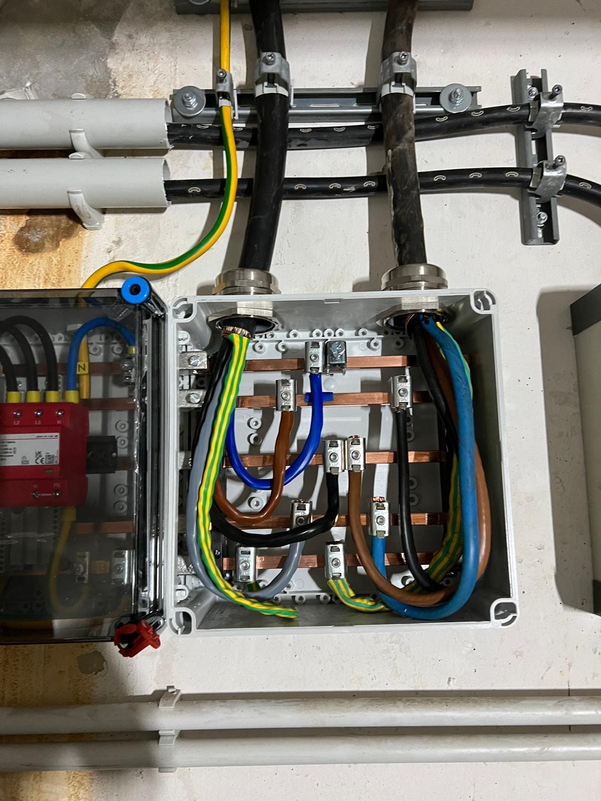 Distribution box with copper bars and connected cables next to an enclosure with surge protection